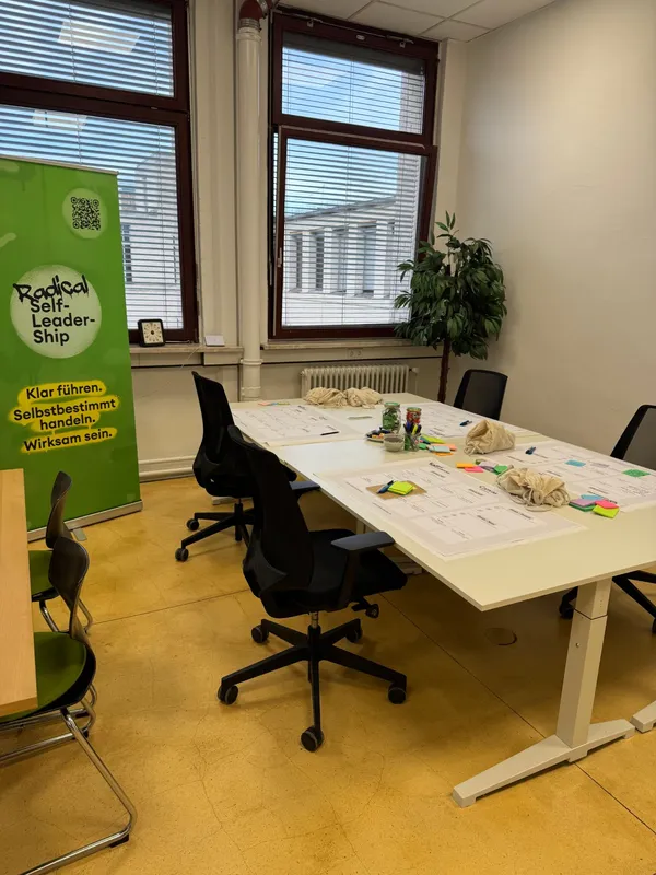 Workshop-Tisch mit ausgelegten Canvas-Bögen, Post-its und Stiften vor dem Radical Self-Leadership Roll-up