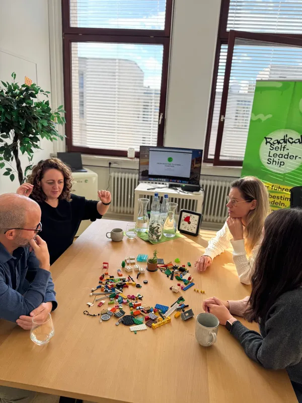Vier Teilnehmende im Gespräch am Tisch mit LEGO-Steinen und Zeitmesser